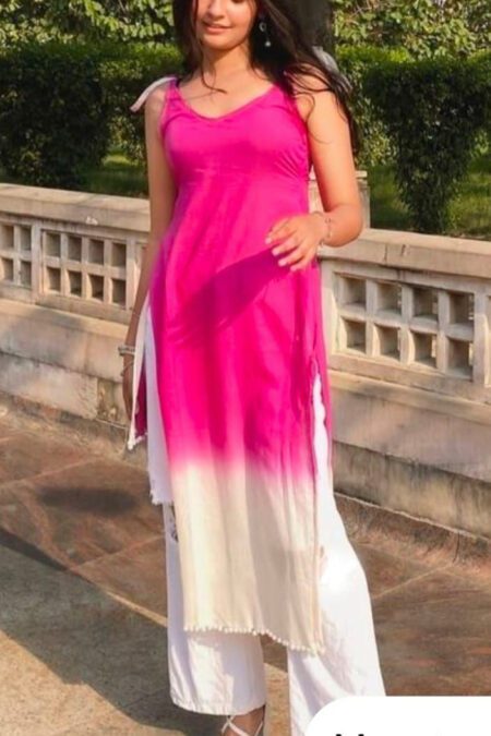 Woman wearing a sleeveless pink-to-white ombre kurti set with white palazzo pants, standing outdoors against a stone railing and lush green background, showcasing a stylish and modern ethnic summer outfit.