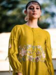 Woman wearing mustard yellow long-sleeve embroidered co-ord with floral thread-work and tassel details, styled with statement earrings and sunglasses for a modern ethnic look.