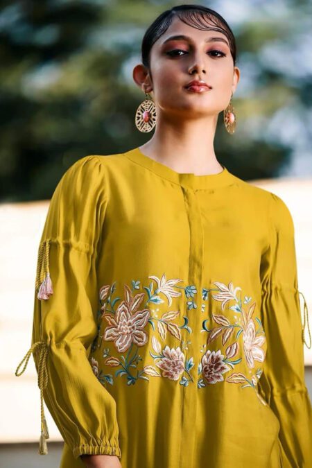 Woman wearing mustard yellow long-sleeve embroidered co-ord with floral thread-work and tassel details, styled with statement earrings and sunglasses for a modern ethnic look.