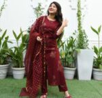 Woman wearing a maroon printed kurta set with matching pants and dupatta, styled for festive or traditional events.