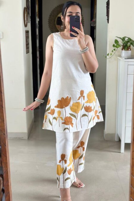 Woman wearing a white sleeveless cotton kurti and pant set with yellow floral prints, ideal for summer ethnic wear and casual styling.
