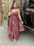 Woman in red printed Anarkali kurta set with dupatta and spaghetti straps, standing stylishly in ethnic festive outfit.