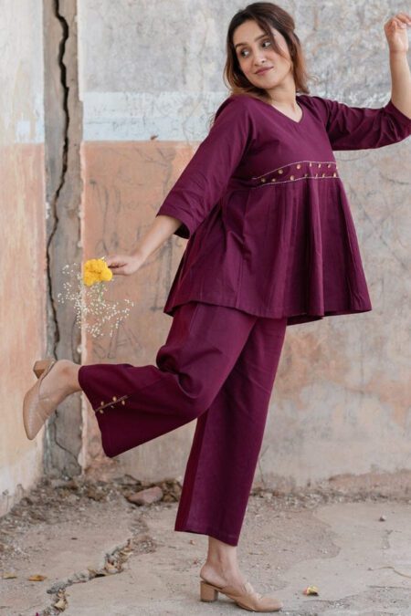 Woman wearing a wine-colored cotton co-ord set with flared top and gold detailing, paired with matching pants – ethnic fusion outfit for daily or festive wear.