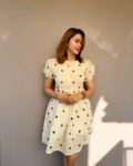 Woman wearing a cute ivory mini dress with red heart prints, puff sleeves, and a cinched waist – perfect for casual wear or summer outings.