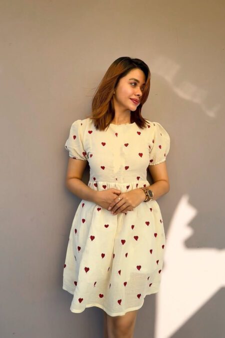 Woman wearing a cute ivory mini dress with red heart prints, puff sleeves, and a cinched waist – perfect for casual wear or summer outings.
