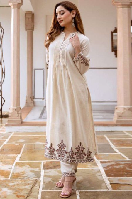 Woman wearing an off-white embroidered kurta with matching pants, posing in a traditional courtyard. The outfit features fine floral threadwork, ideal for festive or formal occasions.