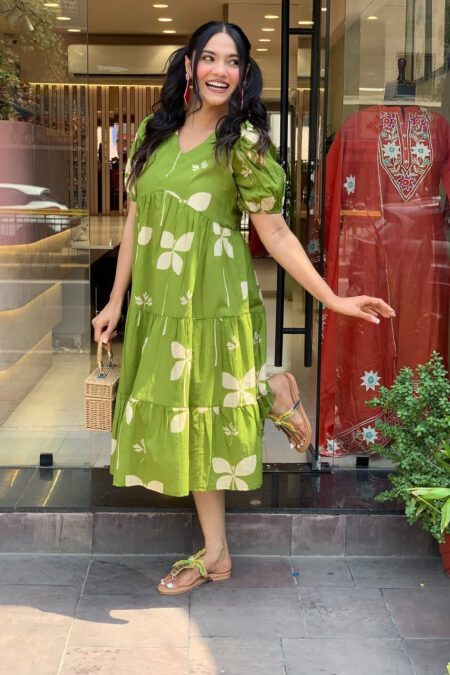 Woman wearing a green floral tiered cotton dress with puff sleeves, styled for summer outing.