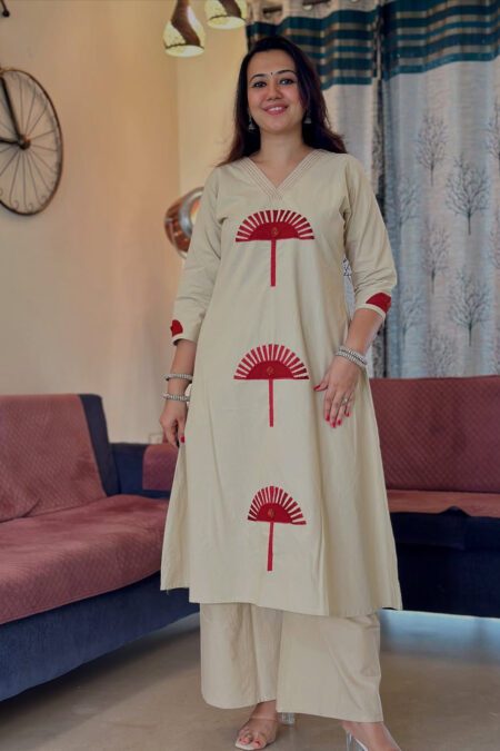 Woman wearing a beige cotton kurta pant set with red fan-style embroidery, standing indoors in a cozy ethnic look perfect for casual or daily wear.