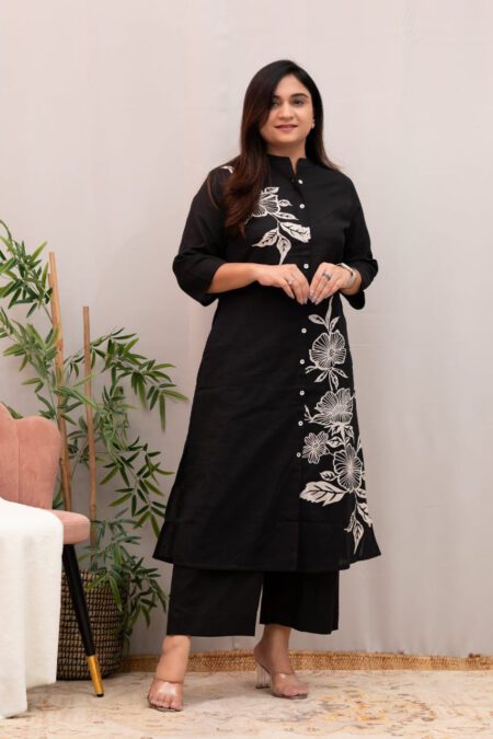 Woman wearing a black cotton kurta with white floral print, front buttons, and matching straight pants – stylish ethnic kurti pant set for women.