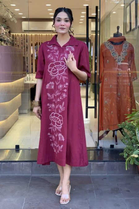 Woman wearing a maroon cotton A-line kurti with floral embroidery, collared neck, and 3/4 sleeves – perfect for ethnic or daily wear.