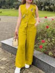 Woman wearing a mustard yellow sleeveless embroidered cotton co-ord set with wide-leg pants in a garden setting.