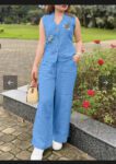Woman in a sky-blue sleeveless cotton kurti-style top with floral embroidery and matching palazzo pants, holding a straw handbag, outdoors with roses in the background.