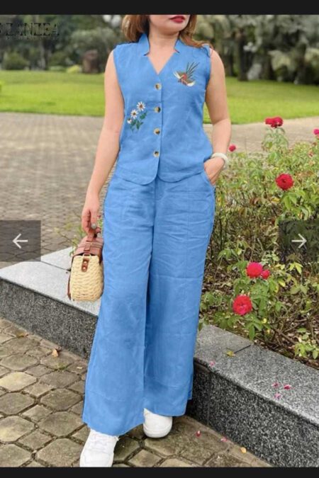Woman in a sky-blue sleeveless cotton kurti-style top with floral embroidery and matching palazzo pants, holding a straw handbag, outdoors with roses in the background.