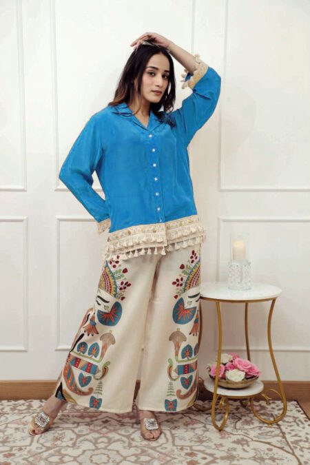 Woman wearing a blue button-down shirt with lace tassel trim and cream wide-leg palazzos with artistic ethnic prints, styled as an Indo-western co-ord set.