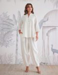 Woman wearing a white full-sleeve co-ord set for women with matching cotton tapered pants, standing confidently against a traditional artistic backdrop.