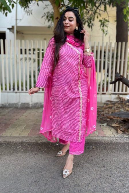 Woman wearing a pink Bandhani print kurti set with golden lace and matching dupatta and pants, styled for festive ethnic look.