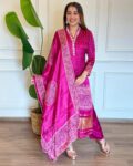Woman wearing a pink Bandhani kurta set with dupatta, adorned with mirror work and traditional prints, ideal for festive and ethnic occasions.