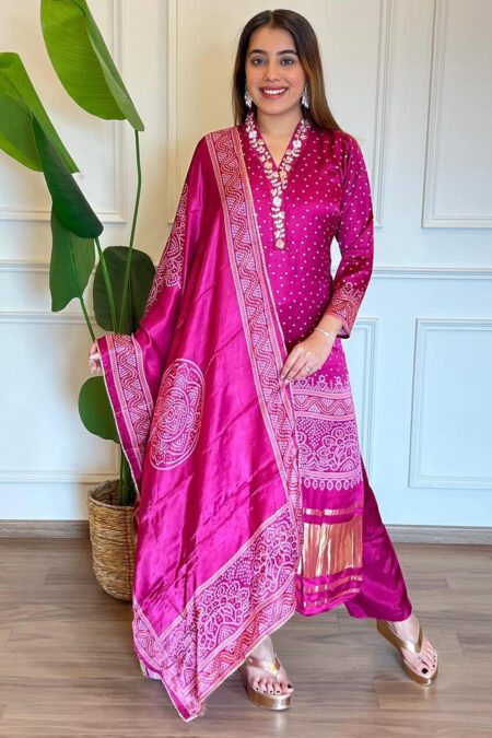 Woman wearing a pink Bandhani kurta set with dupatta, adorned with mirror work and traditional prints, ideal for festive and ethnic occasions.