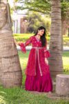 Woman wearing a vibrant pink Bandhani printed kurta with flared skirt, styled for festive ethnic occasions under a tree setting.